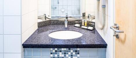Un baño con lavamanos de encimera de granito, espejo y salpicadero de azulejos.