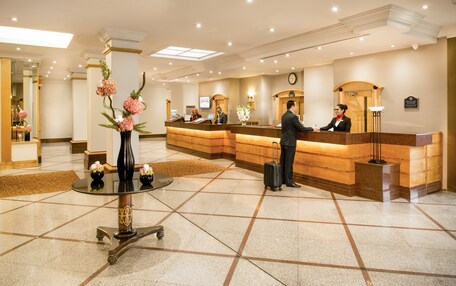 A hotel reception area with a reception desk, a clock, and a vase with flowers.