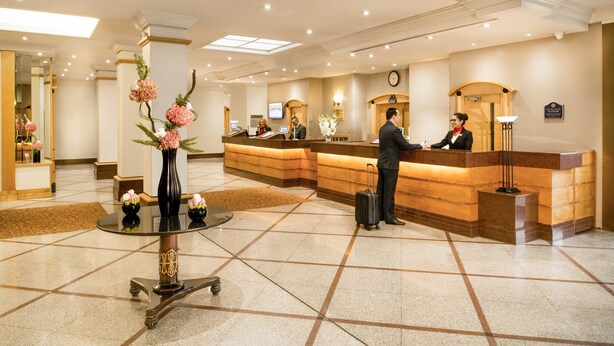 Zona de recepción de hotel con mostrador, un reloj y un jarrón con flores.