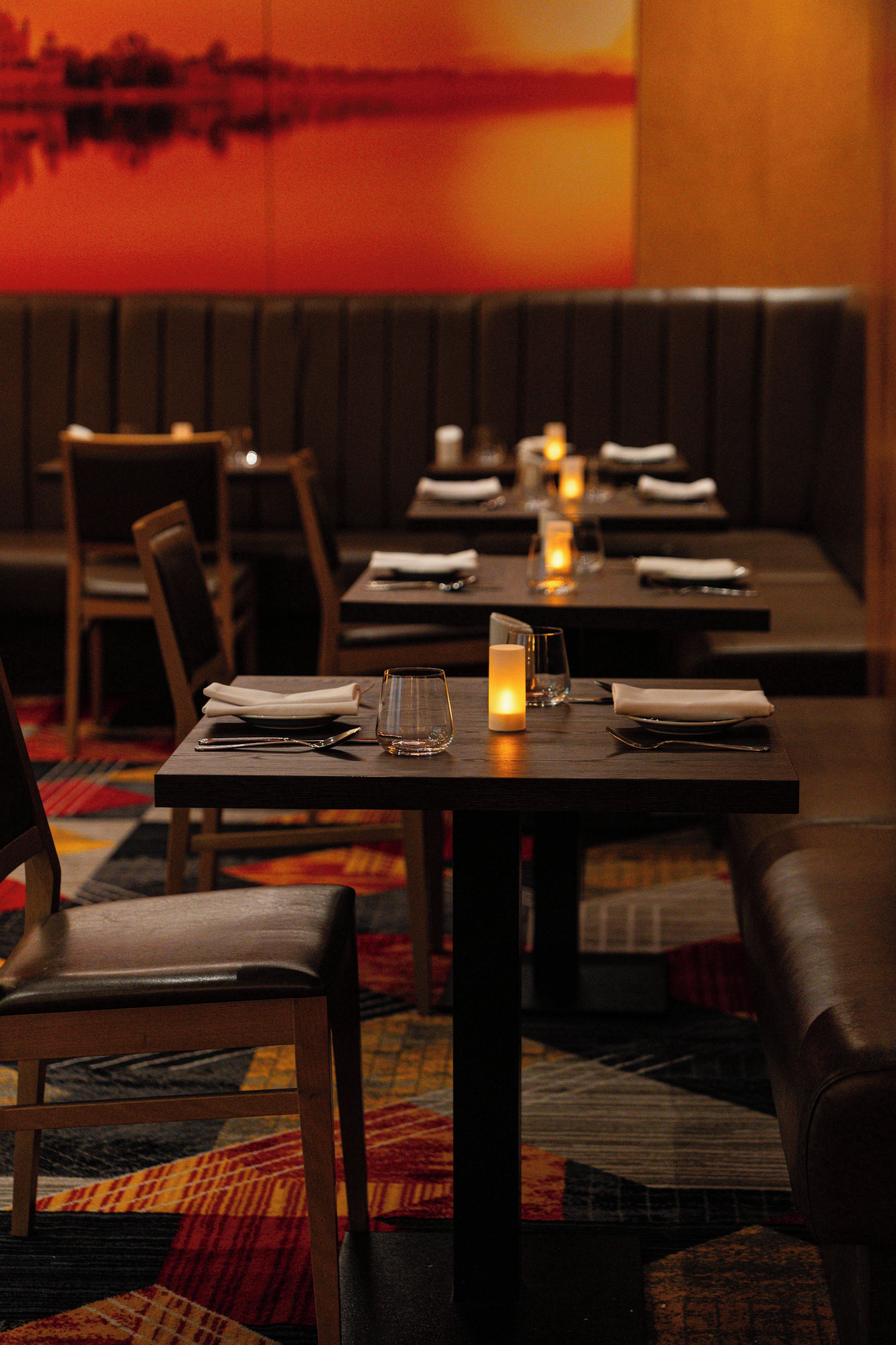 A restaurant with booths and tables, each set with cutlery, glasses, and candles.