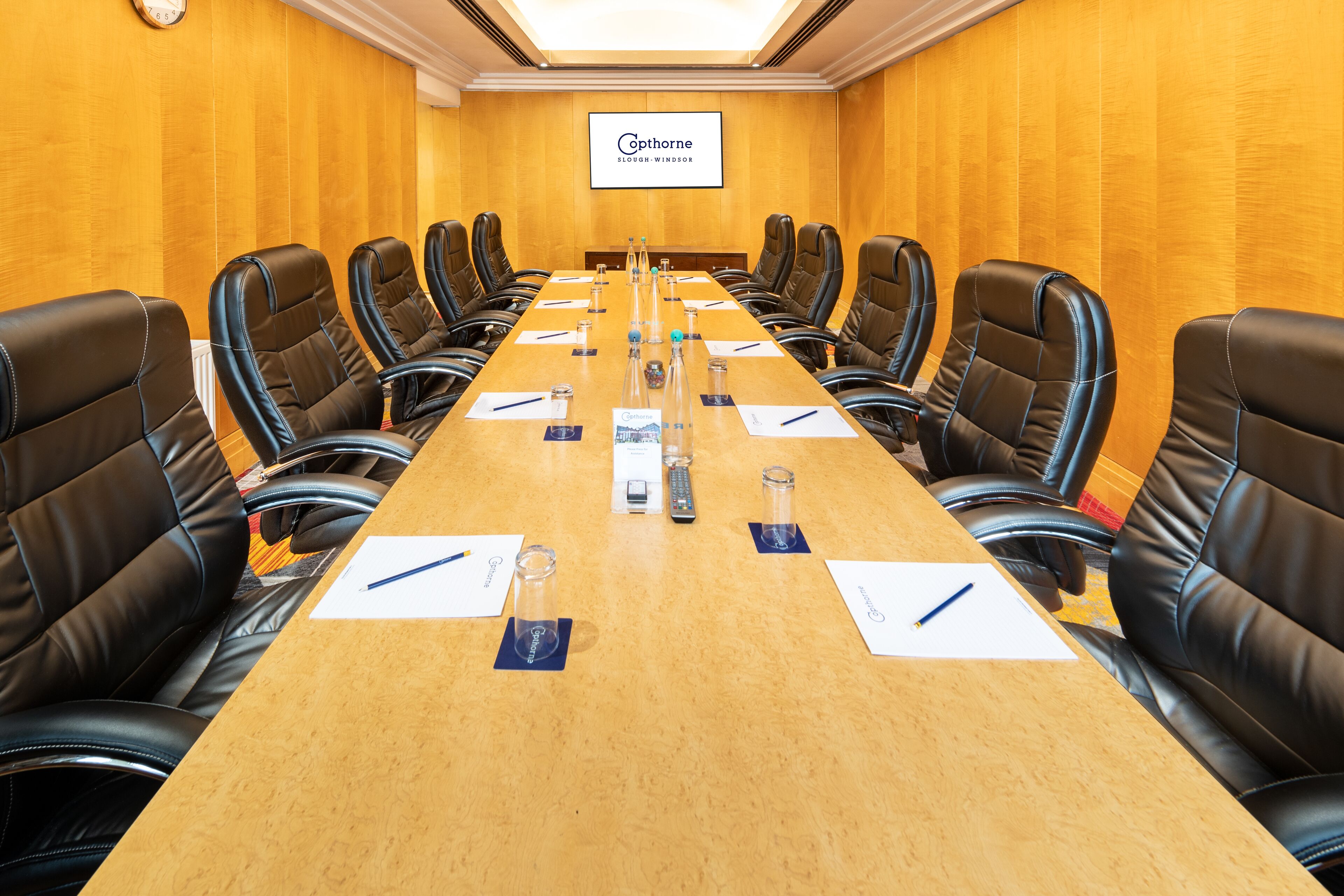A conference room with a long table, black leather chairs, and a screen displaying the name 'Cophorne Slough Windsor'.