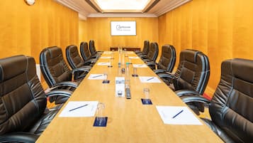A conference room with a long table, black leather chairs, and a screen displaying the name 'Cophorne Slough Windsor'.