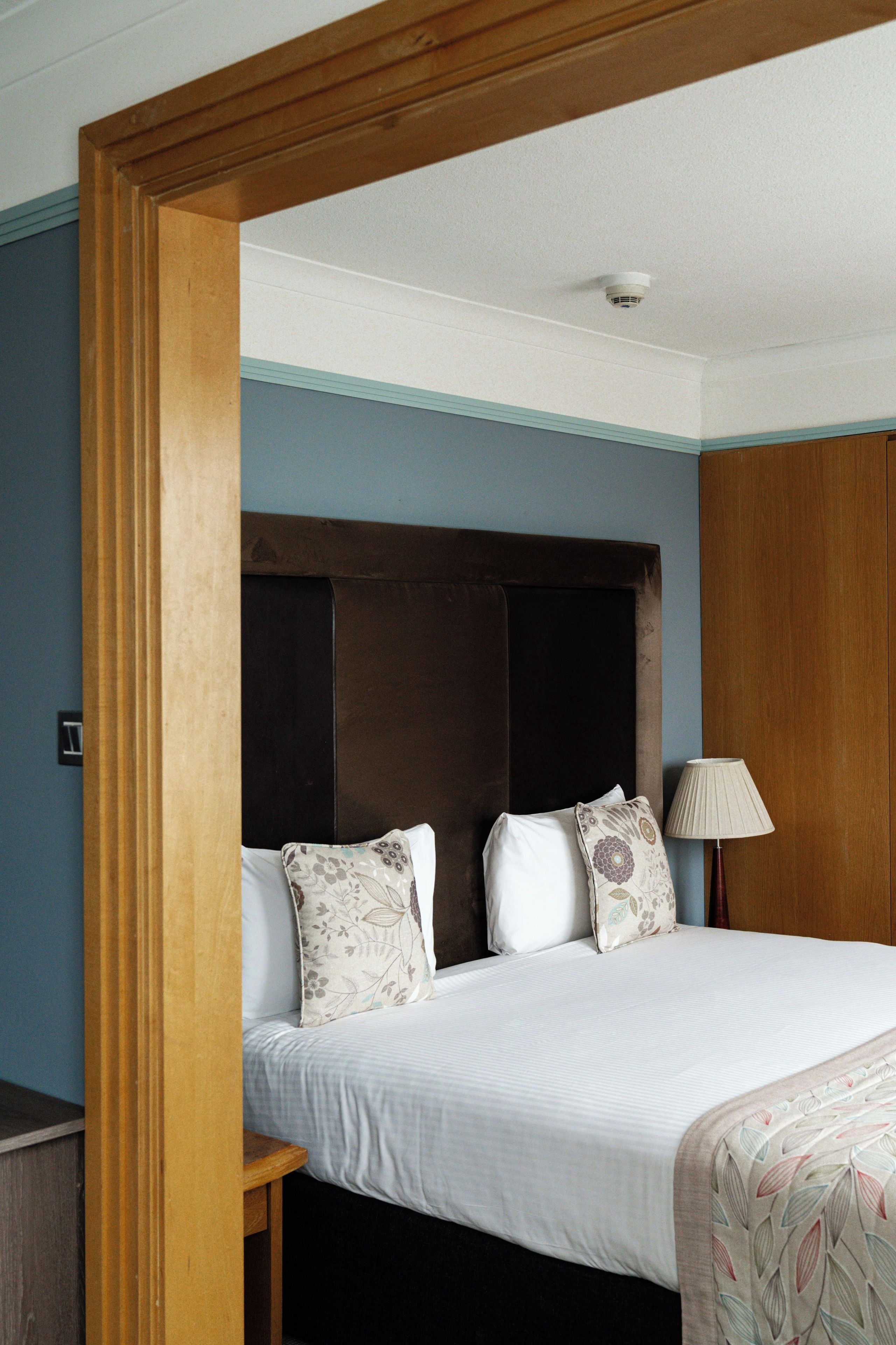 A hotel room with a bed, a nightstand, a lamp, and a wooden headboard.