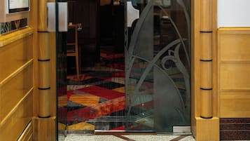 Una entrada a un edificio con la leyenda 'Bombay Pavilion', con una puerta de cristal que presenta ornamentación metálica intrincada.