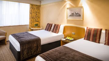 A hotel room with two beds, a small round table with a vase of flowers, and a framed picture on the wall.