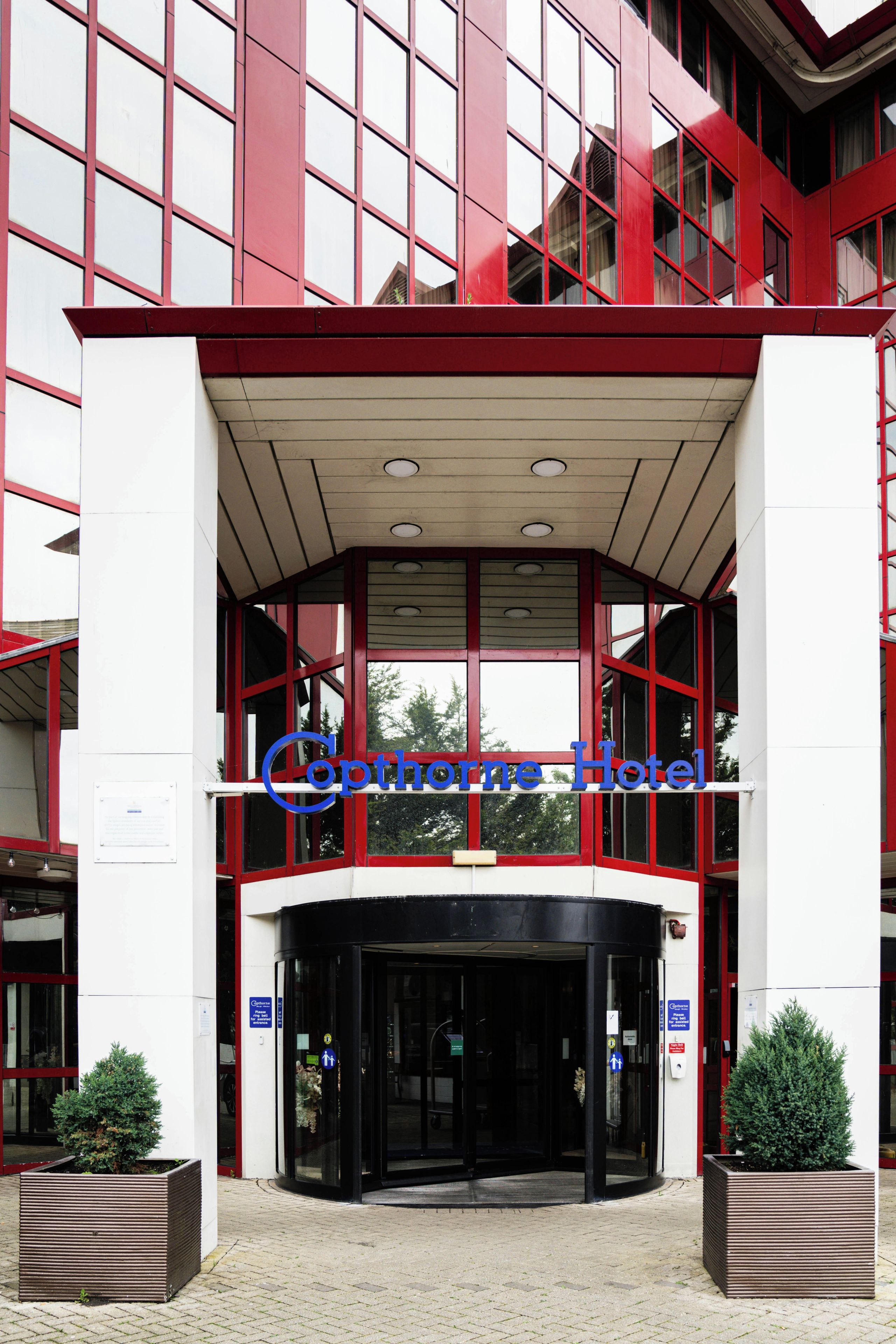 A hotel entrance with a revolving door, a sign above the door, and a potted plant on the left.