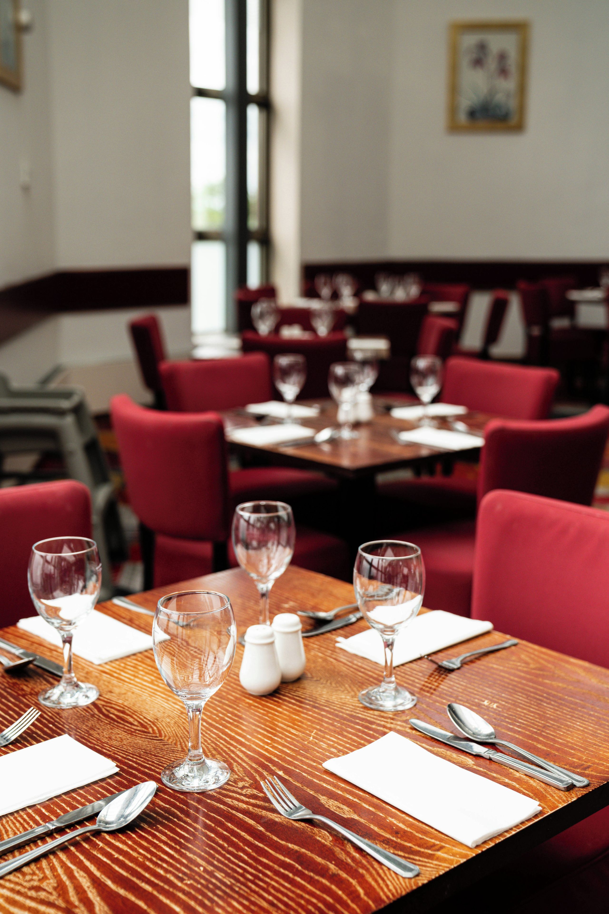 L’intérieur d’un restaurant avec des chaises à revêtement rouge, des tables en bois, ainsi que des verres à vin et des couverts vides.