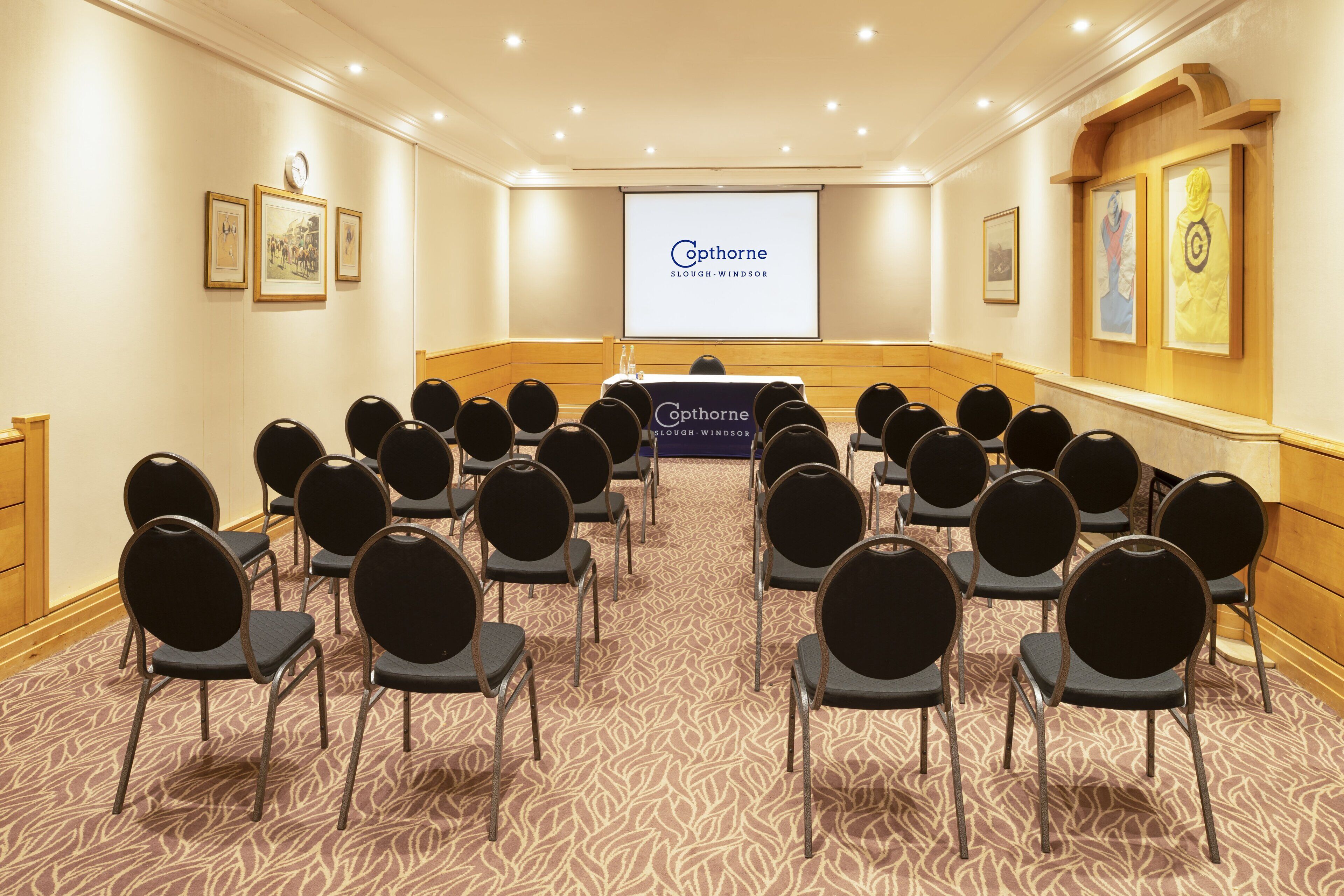 A conference room with rows of chairs facing a presentation screen, a podium, and framed artwork on the walls.