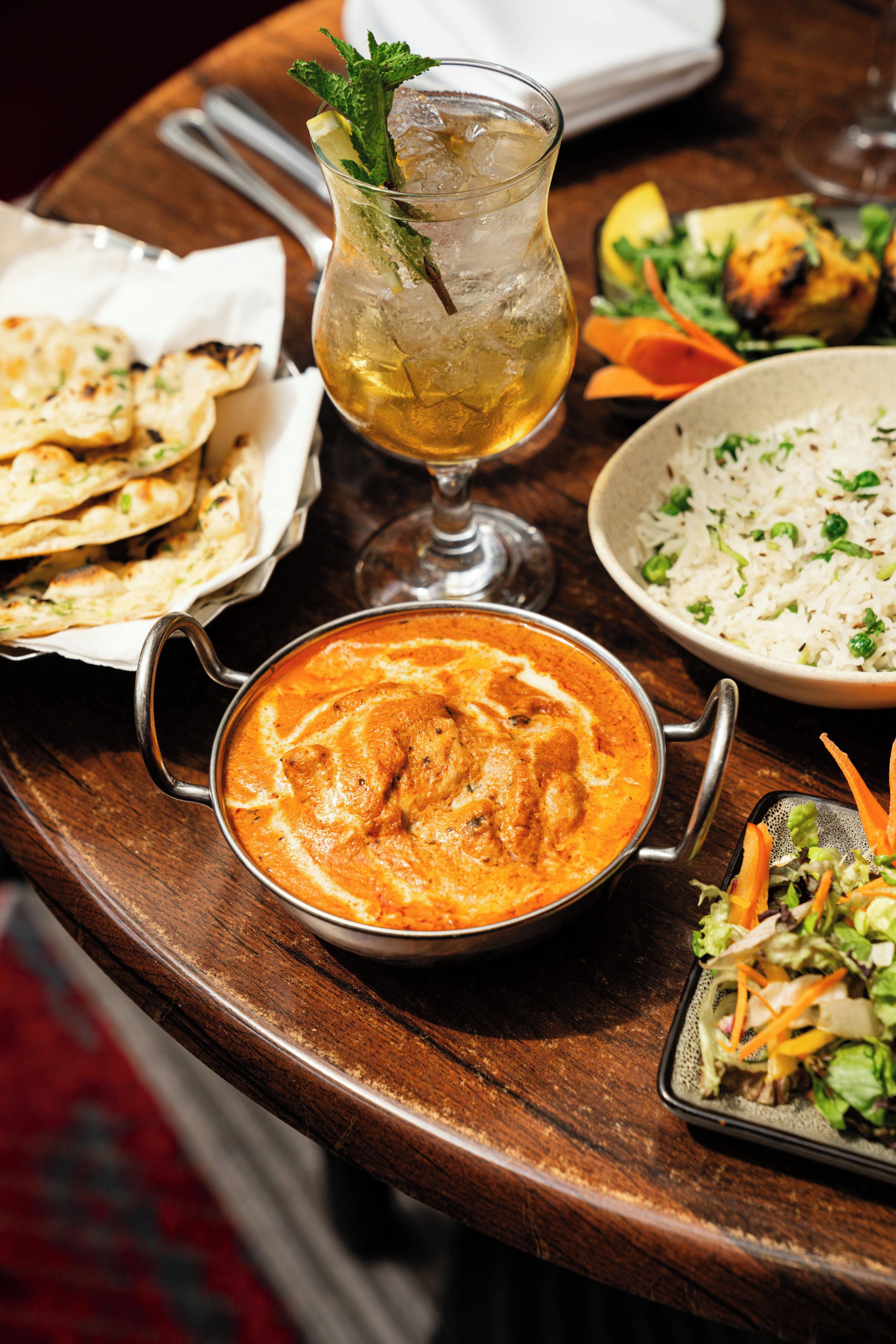 A table with a variety of dishes including a bowl of curry, a plate of rice, a salad, and some flatbread.