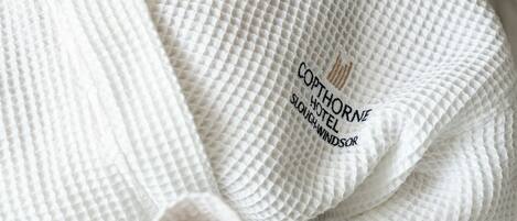 A person in a white bathrobe holding a cup, with a hotel name embroidered on the robe.