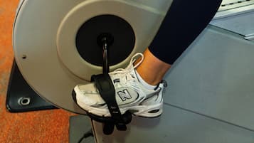 Una bicicleta estática de ejercicio con el nombre de la marca visible, las piernas de una persona con ropa deportiva y una parte del suelo cubierto de alfombra.