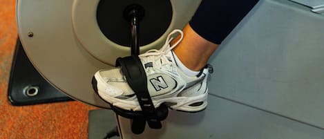Una bicicleta estática de ejercicio con el nombre de la marca visible, las piernas de una persona con ropa deportiva y una parte del suelo cubierto de alfombra.