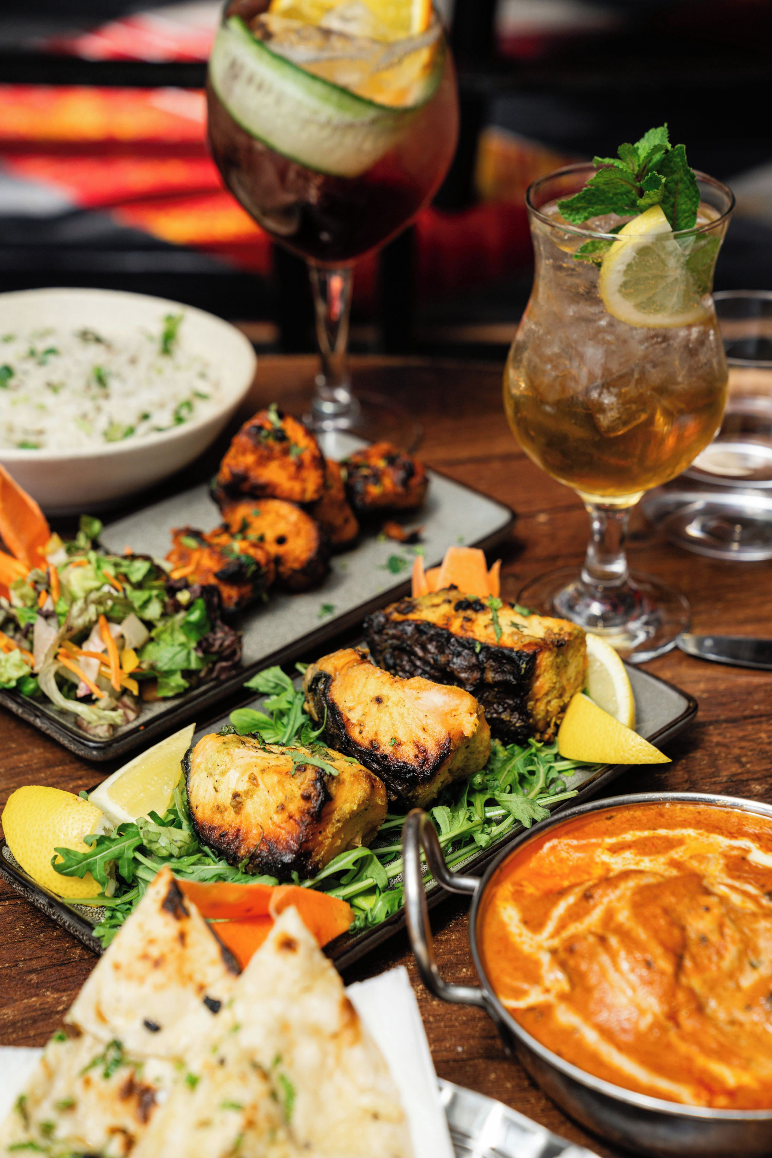 A variety of dishes including grilled chicken, a bowl of curry, and a glass of iced tea on a wooden table.