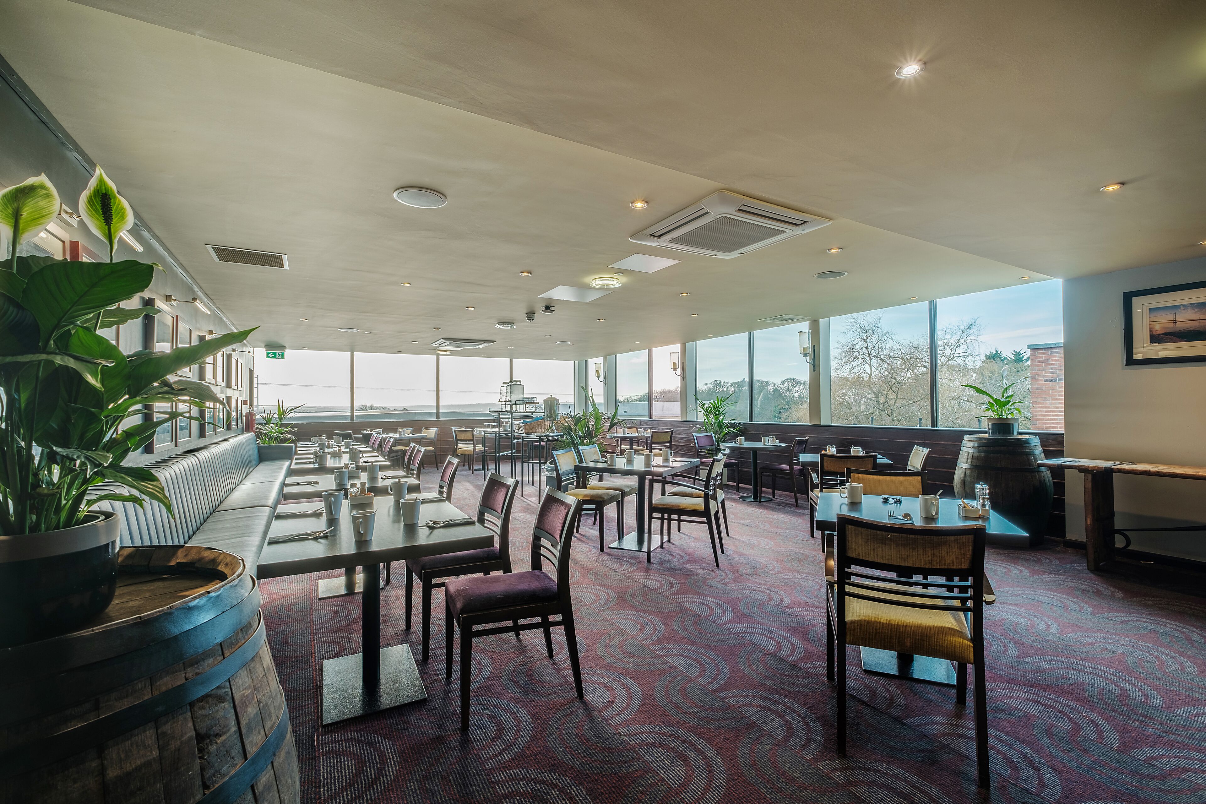 Un restaurante espacioso con techos altos, amplias ventanas y diversas opciones de asientos, incluyendo mesas y cabinas.