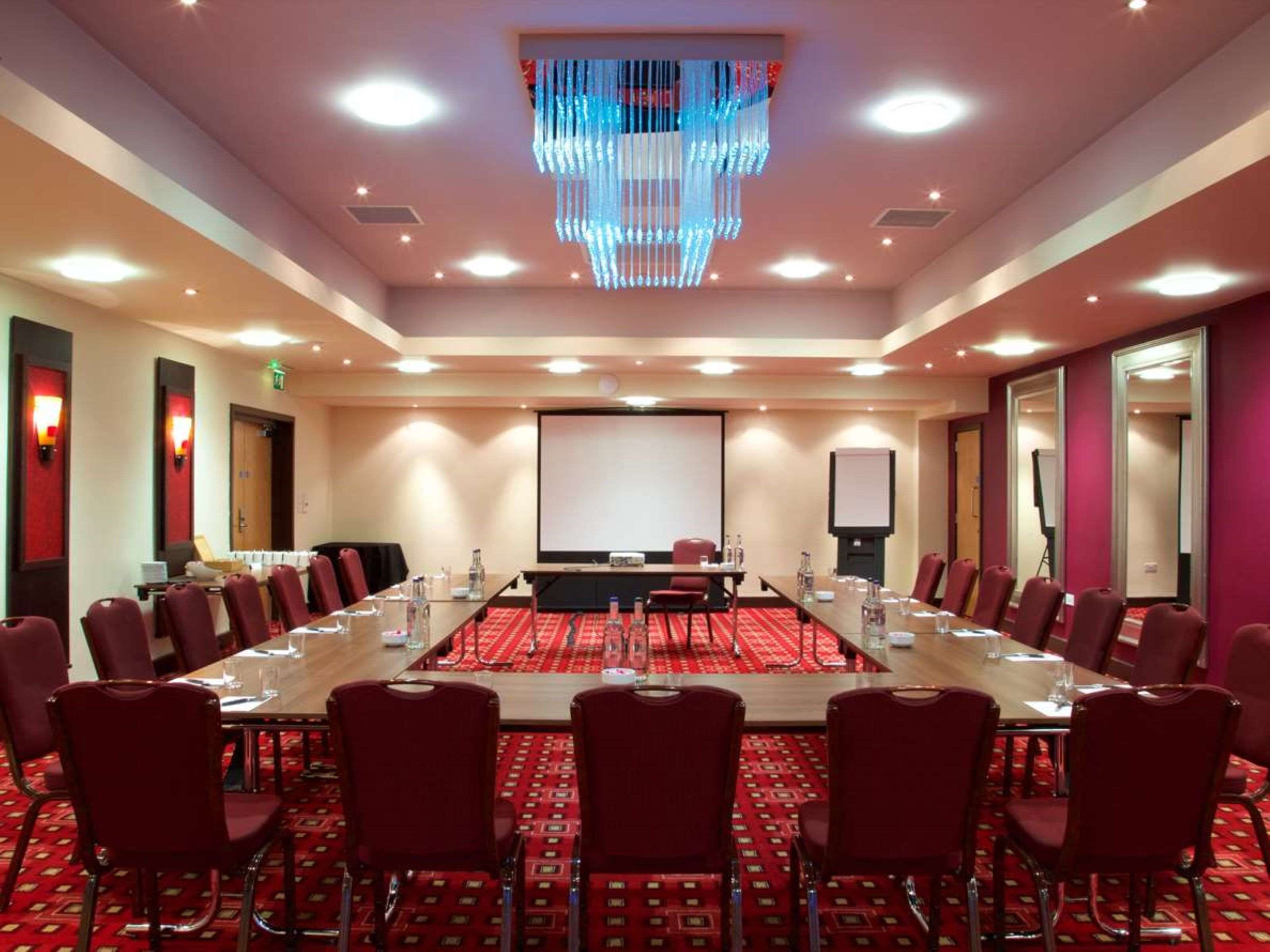 A conference room with a long table, red carpet, and red chairs.