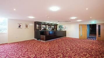 A spacious room with a red patterned carpet, a reception desk, and a staircase leading to another floor.