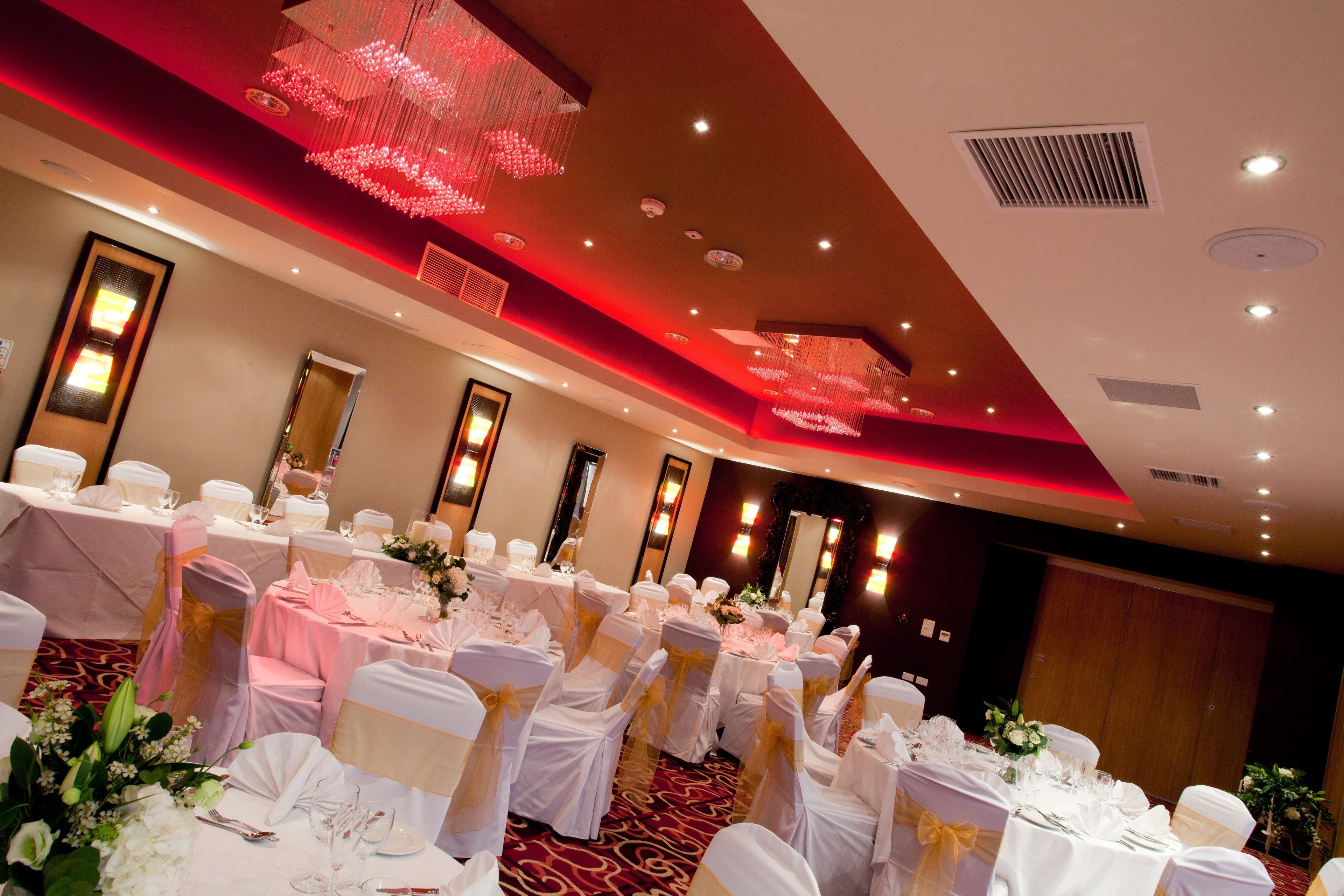 A banquet hall with round tables, white tablecloths, and chairs with gold sashes.