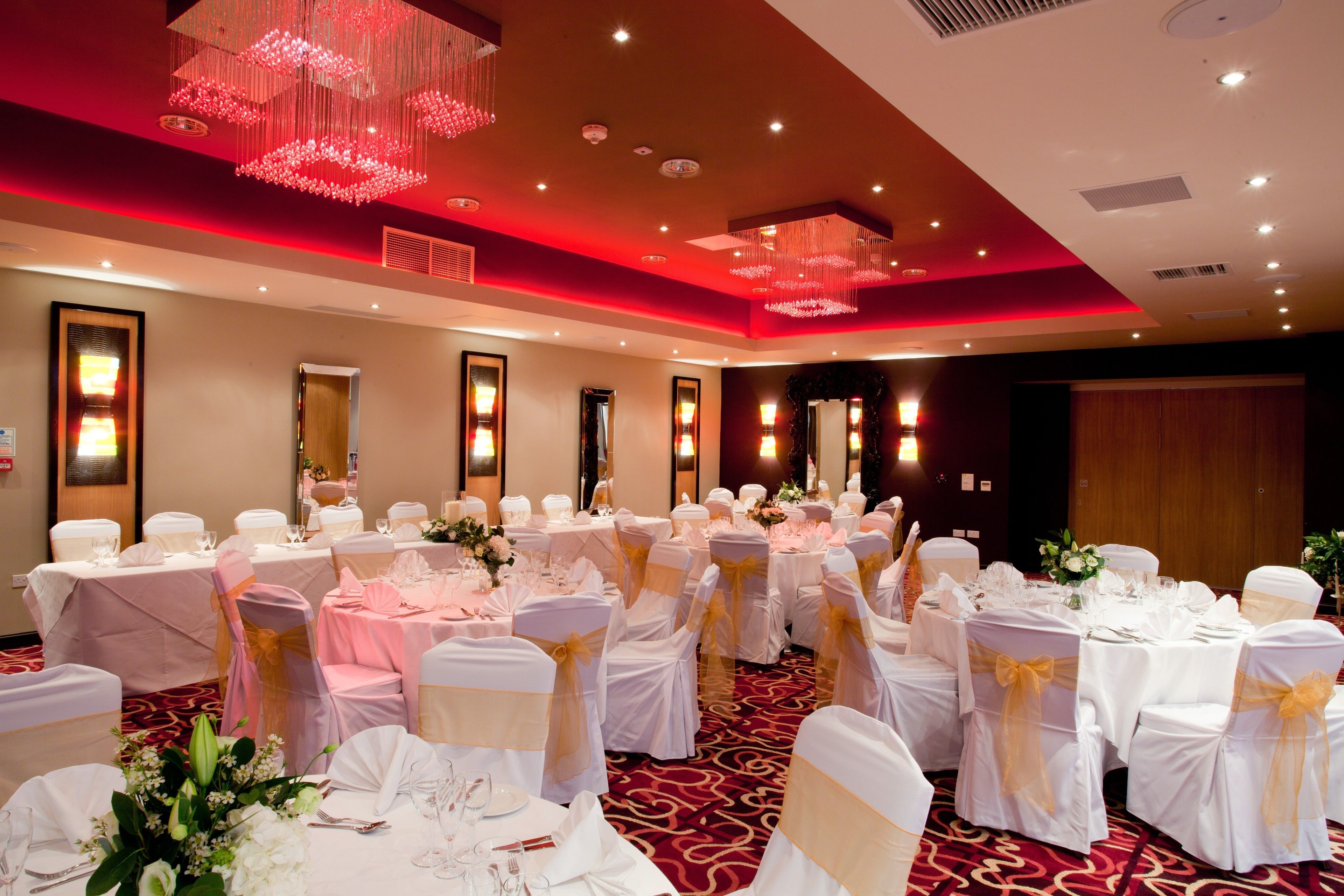 A banquet hall with round tables, white tablecloths, and chairs with gold sashes.