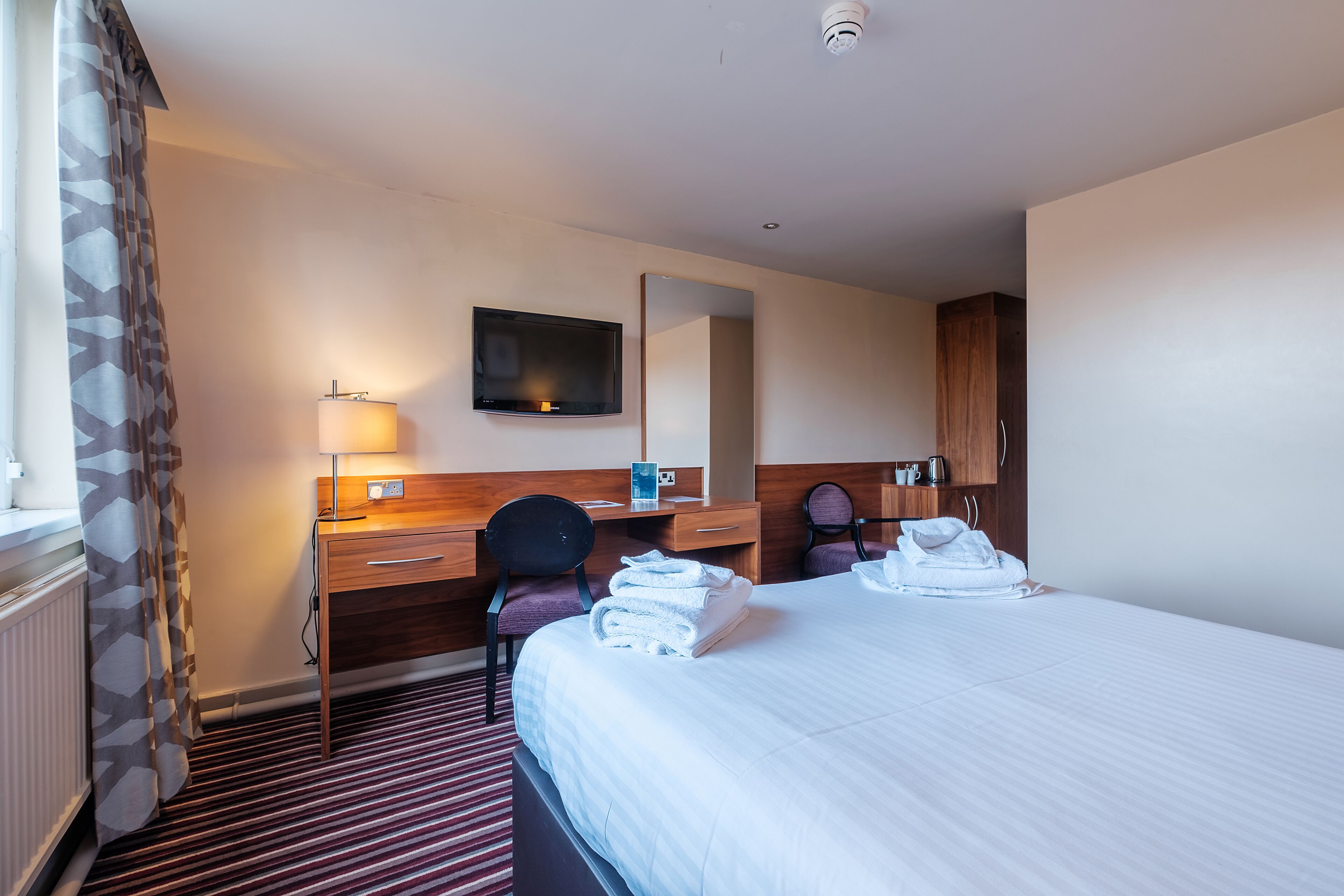 Een hotelkamer met een bed, een bureau, een stoel, een televisie en een spiegel.