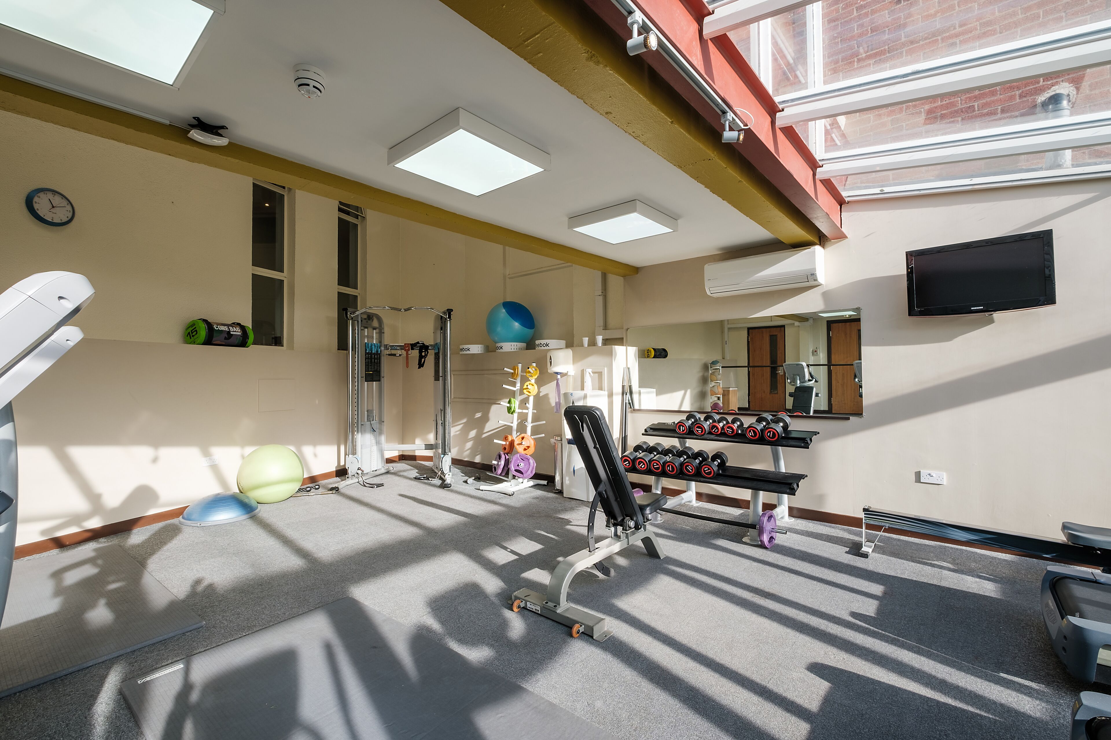 Ein Fitnessraum mit Trainingsgeräten, einem Spiegel und einem Fernseher an der Wand.