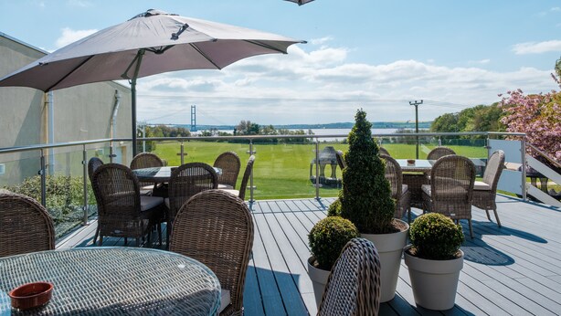 A deck with wicker furniture and a large umbrella, overlooking a green landscape and a bridge. - Hull Humber View Hotel, Sure Hotel Collection by BW (North Ferriby)
