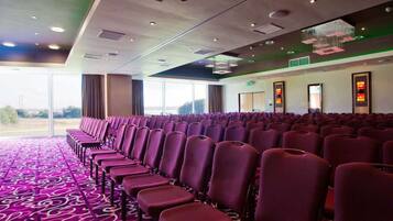 A conference room with rows of purple chairs, a patterned carpet, and large windows offering a view of the outdoors.