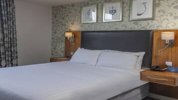A neatly made bed with white linens, a wooden headboard, two bedside tables with lamps, and a wall with three framed pictures.