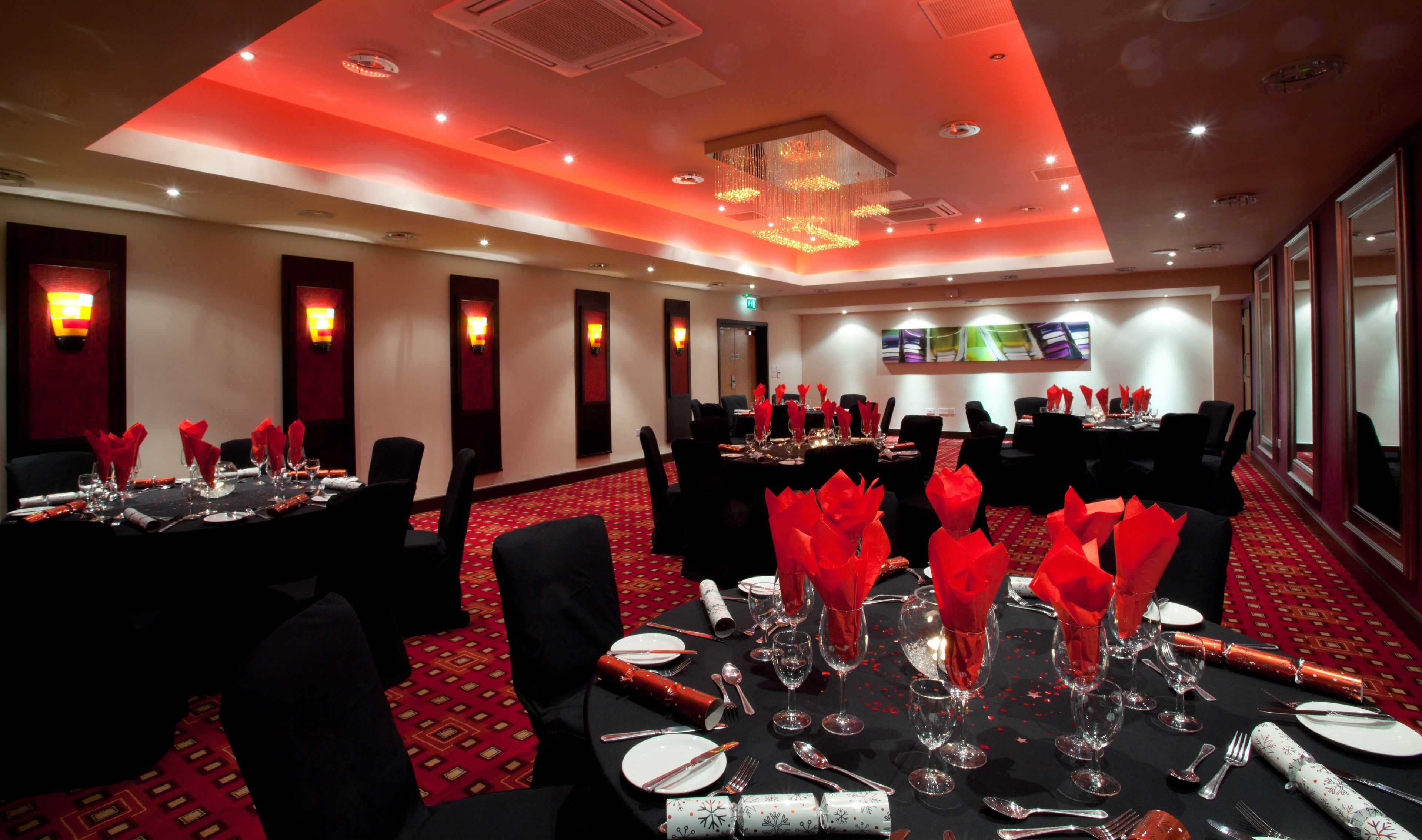A conference room with tables set for a formal event, equipped with chairs, tables, and a large screen.
