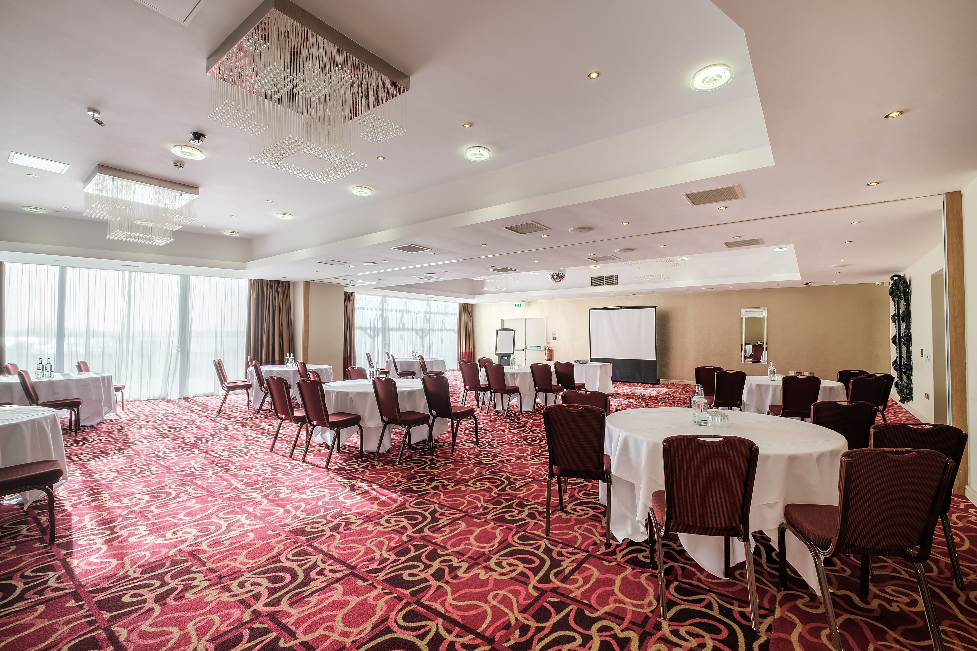 A conference room with round tables, chairs, and a carpeted floor.