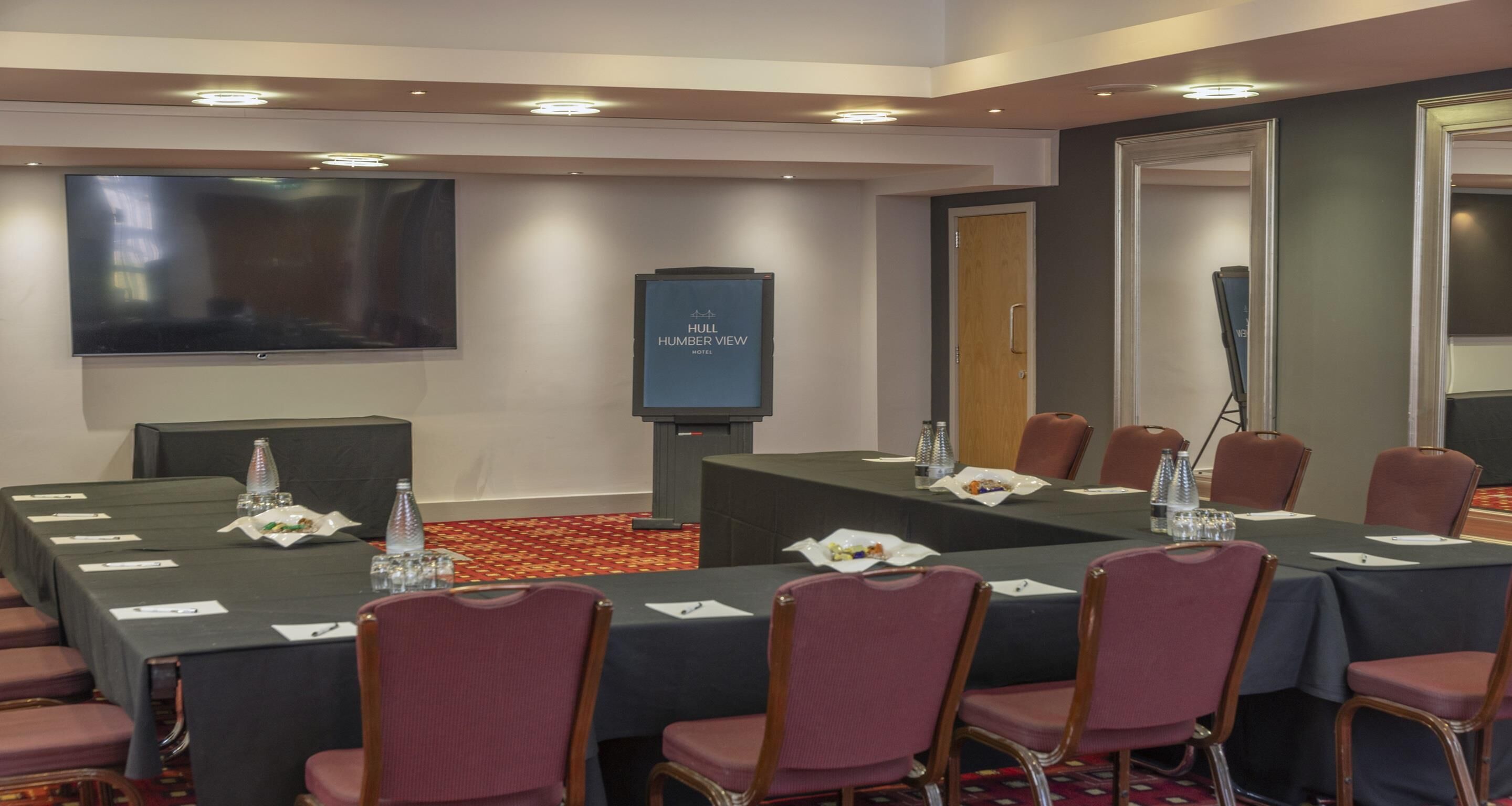 Un salón de conferencias con una gran mesa, sillas, un televisor de pantalla plana y un cartel que dice "HULL HUMBERT VIEW HOTEL".