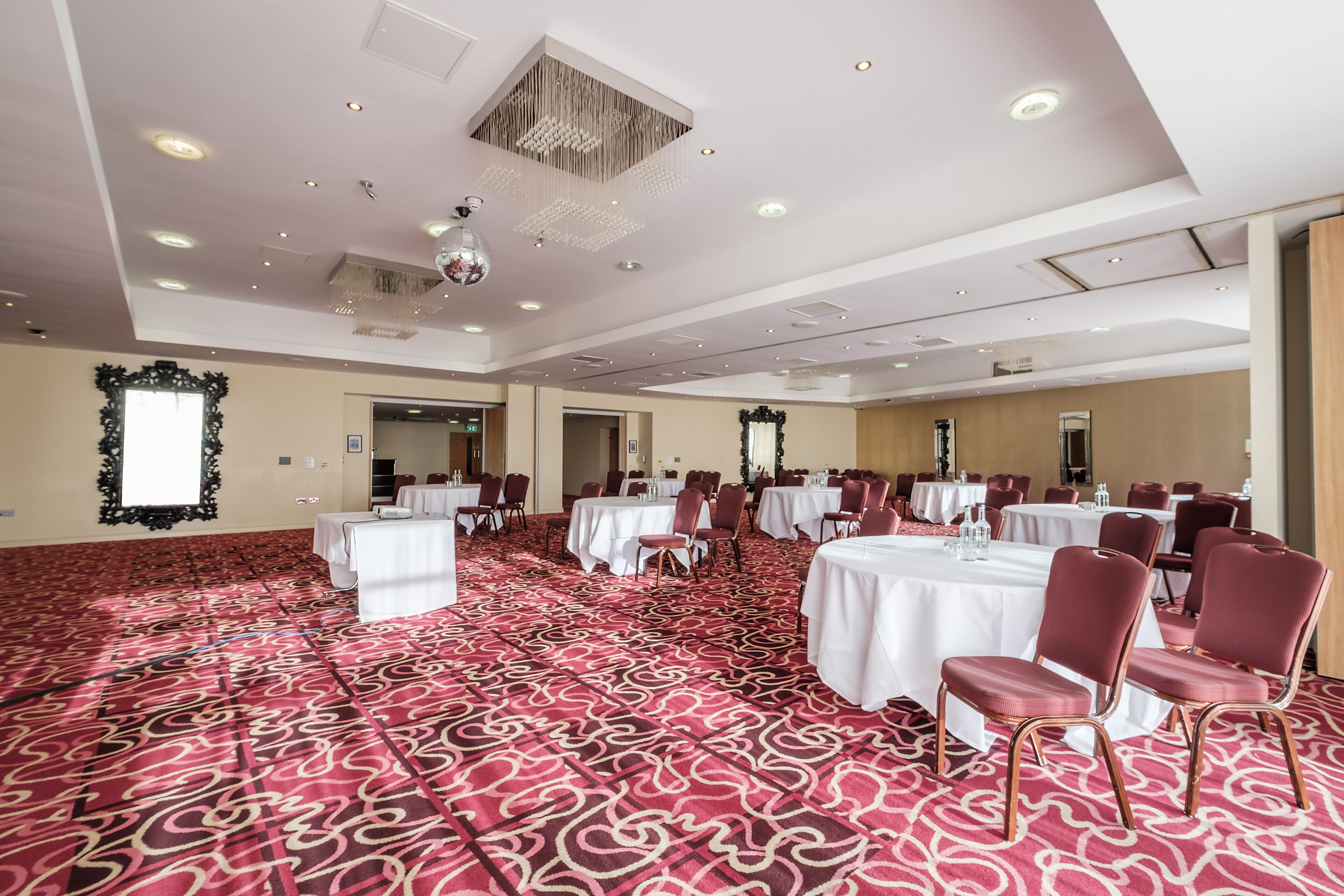 Un salón de conferencias con mesas y sillas, una alfombra estampada y un candelabro.