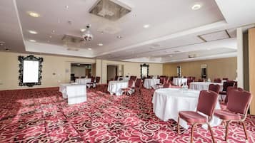Un salón de conferencias con mesas y sillas, una alfombra estampada y un candelabro.