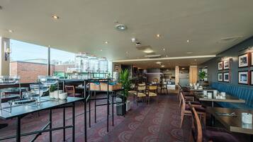 A spacious restaurant with high tables and chairs, a bar area, and a seating section with a blue booth.