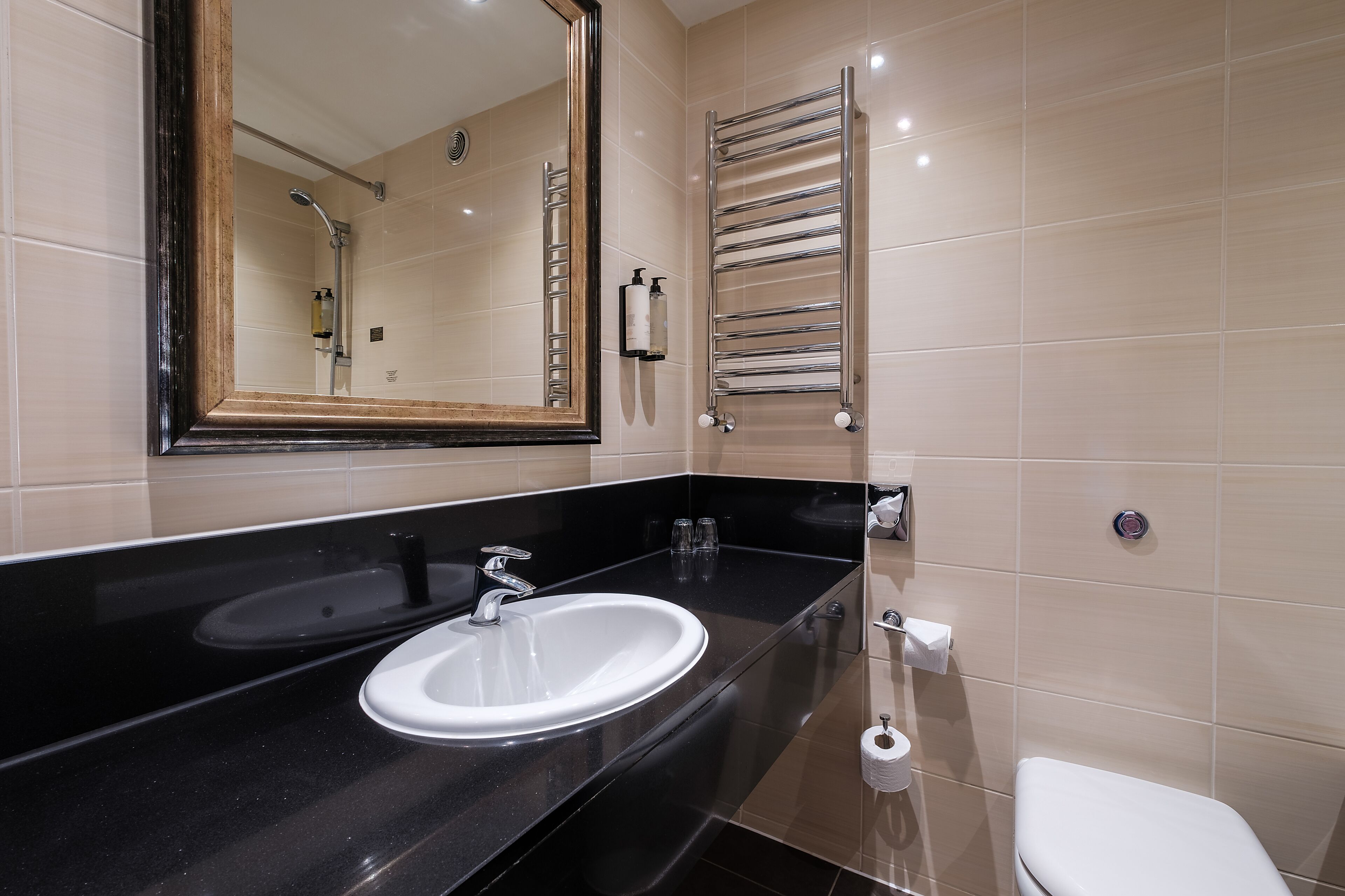 A modern bathroom with a black sink, a mirror, a towel rack, and a toilet.
