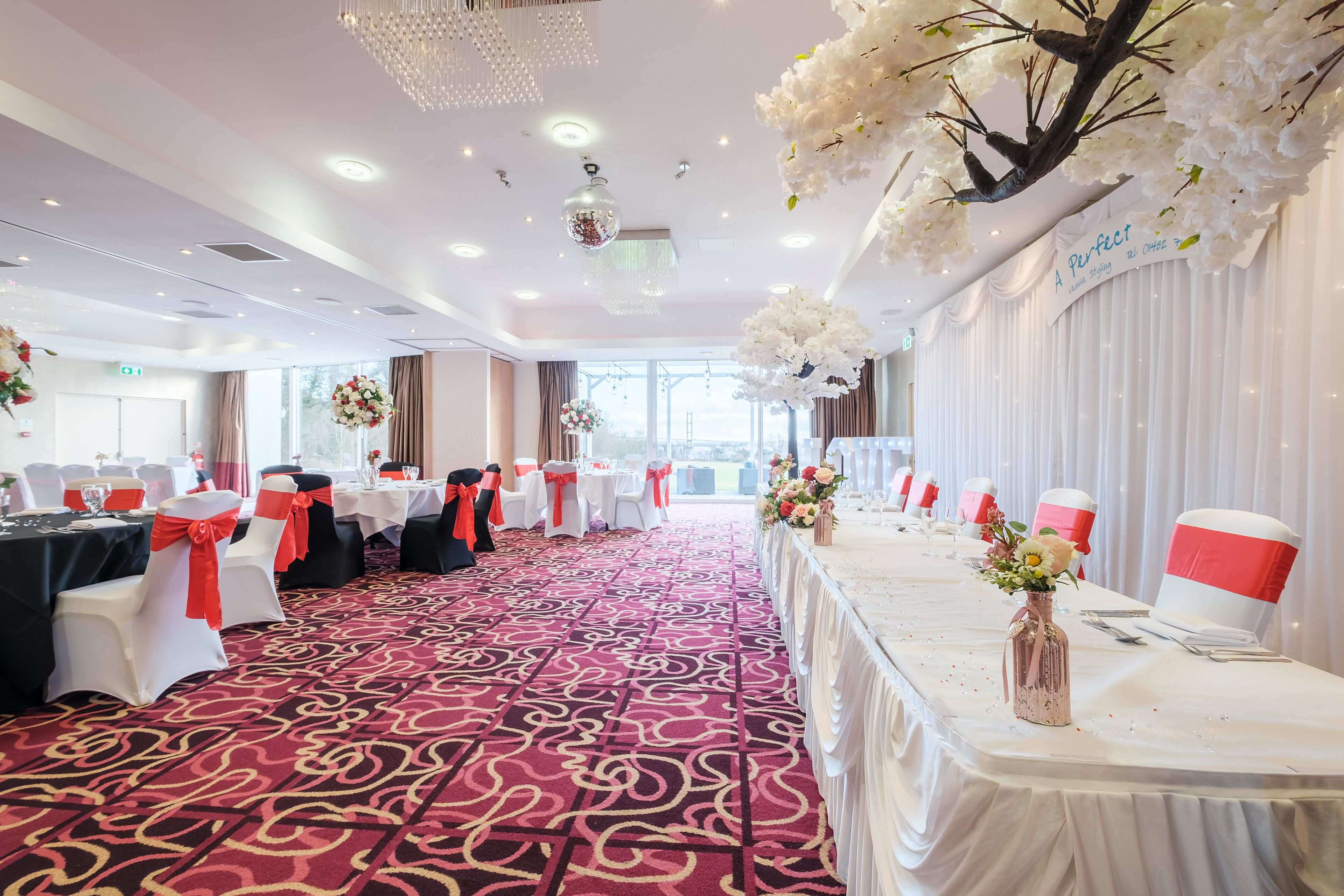 A banquet hall with tables set for a formal event, featuring a red carpet and white drapery.