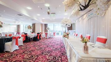 A banquet hall with tables set for a formal event, featuring a red carpet and white drapery.
