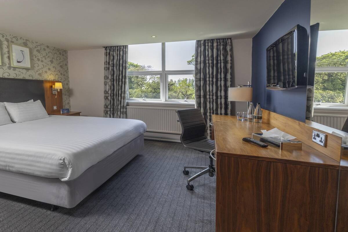 Une chambre d’hôtel avec un grand lit, un bureau avec une télévision et des œuvres d’art encadrées au mur.
