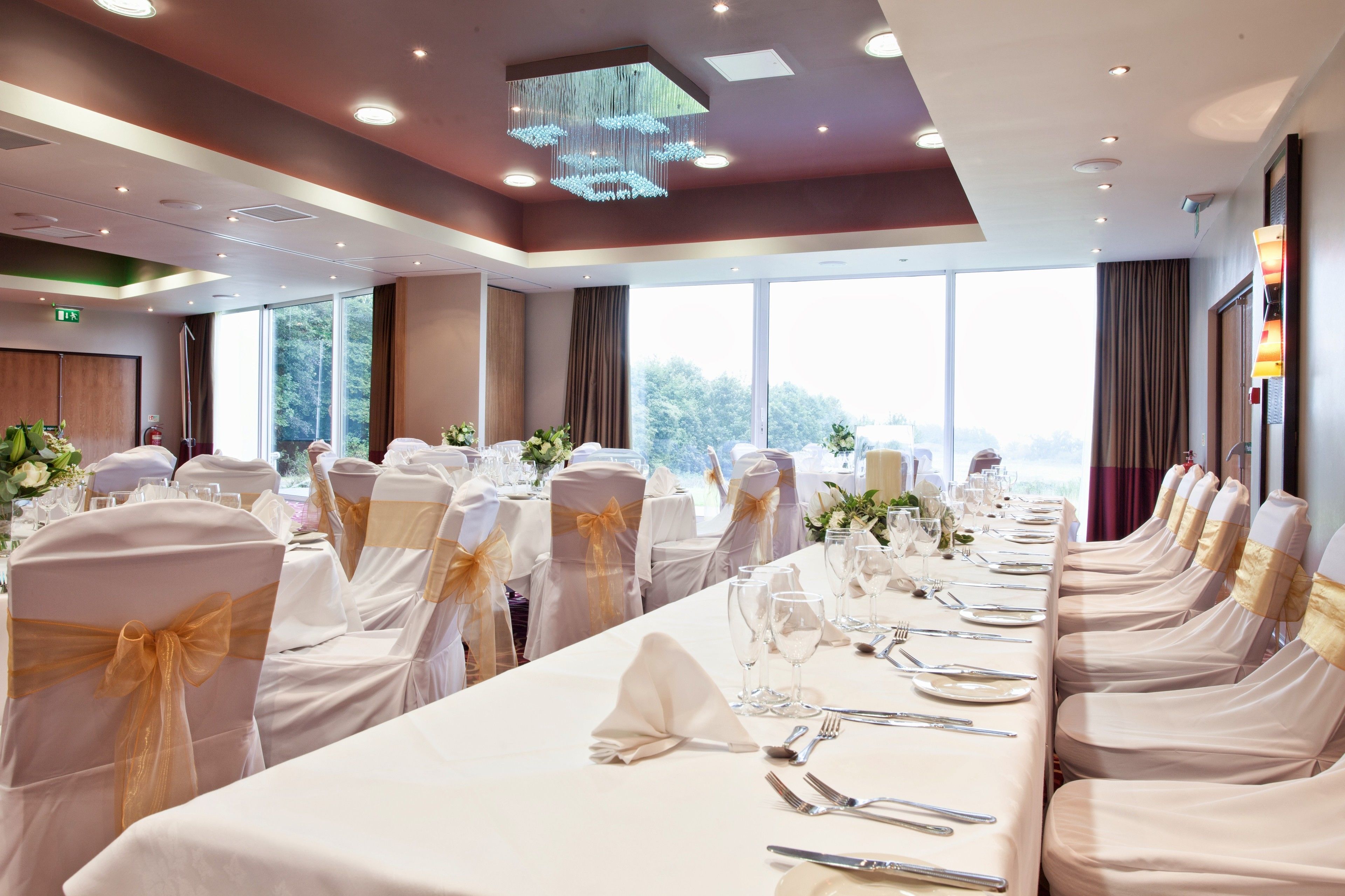 A banquet hall with long tables, chairs with gold sashes, and a chandelier.