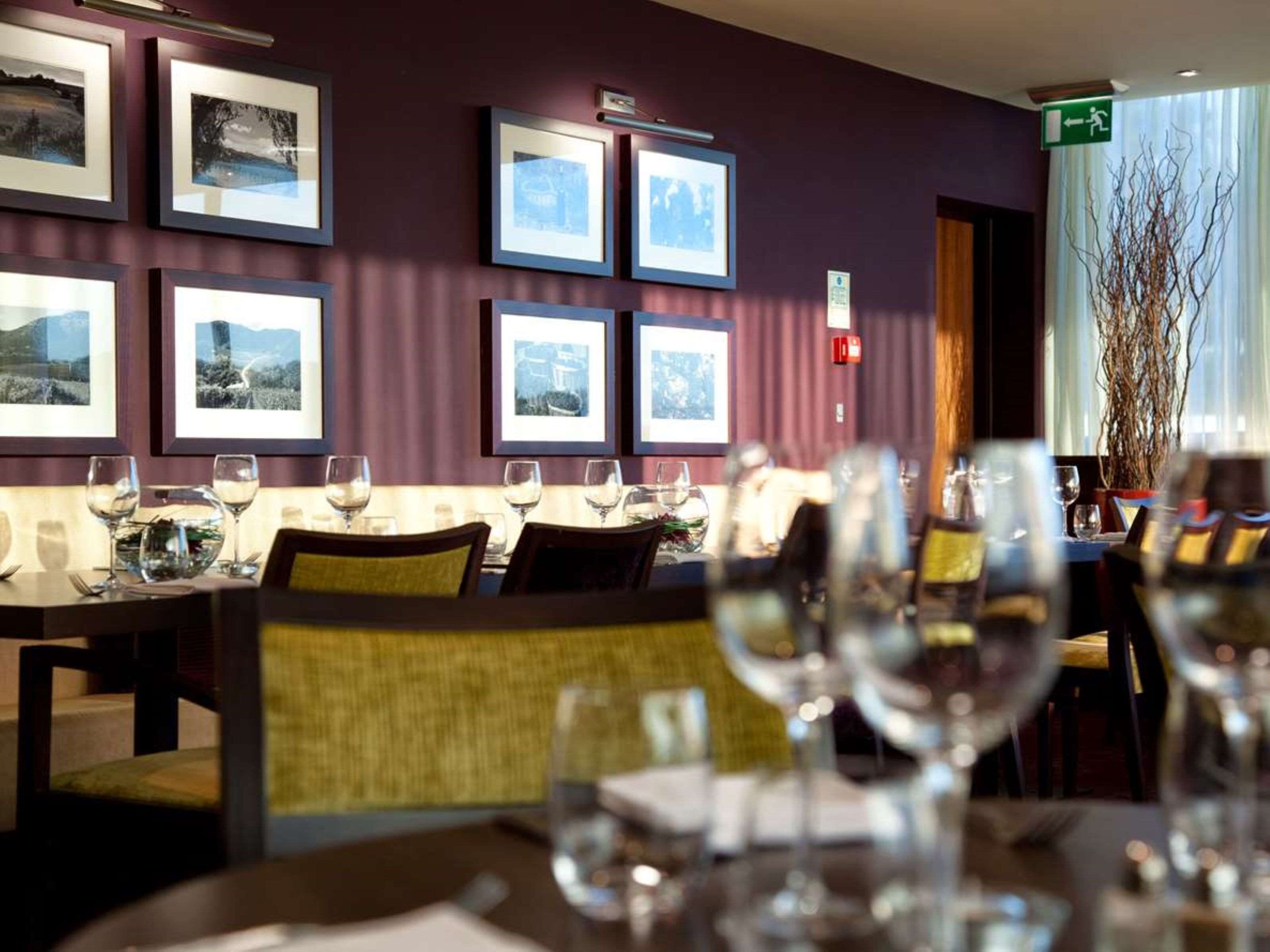 Ein Restaurant mit gerahmten Bildern an der Wand, Tischen mit Weingläsern und einem grünen Fluchtwegschild.