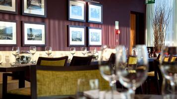 Ein Restaurant mit gerahmten Bildern an der Wand, Tischen mit Weingläsern und einem grünen Fluchtwegschild.