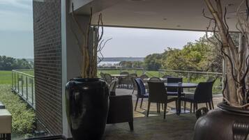 Un patio al aire libre con una mesa y sillas, un gran jarrón negro con ramas, y vista a un paisaje verde.