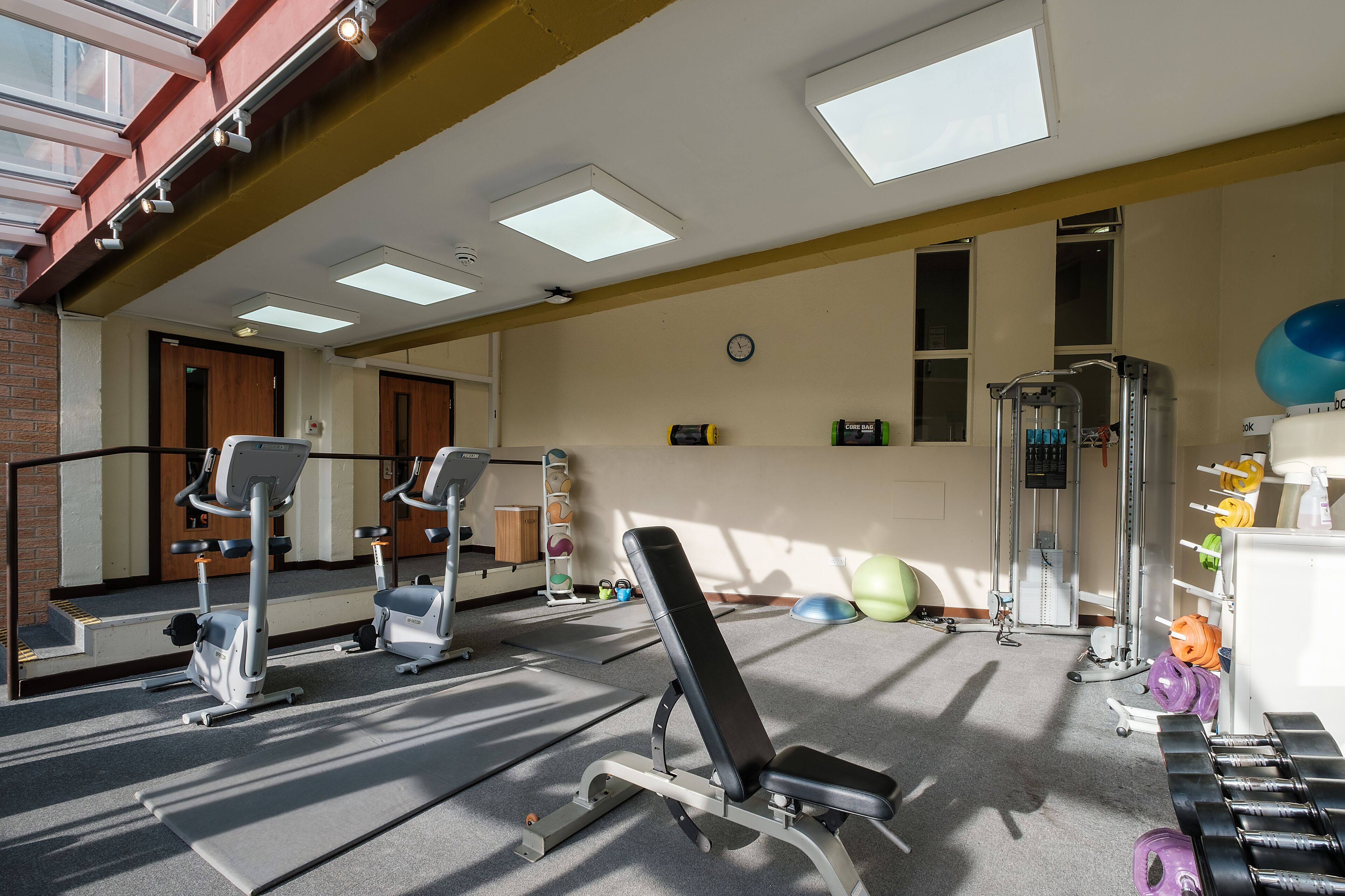 Uma academia com equipamentos de exercício, um relógio e uma janela.