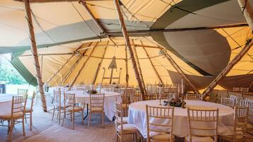 A large, open tent with multiple round tables and chairs, set up for dining or events.