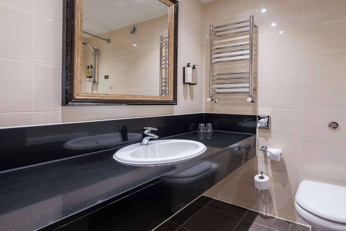 Une salle de bain moderne avec un plan de toilette noir, deux vasques, un miroir, un porte-serviettes et des toilettes.