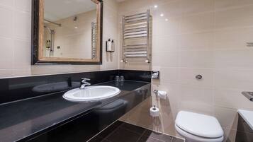 A modern bathroom with a black countertop, two sinks, a mirror, a towel rack, and a toilet.