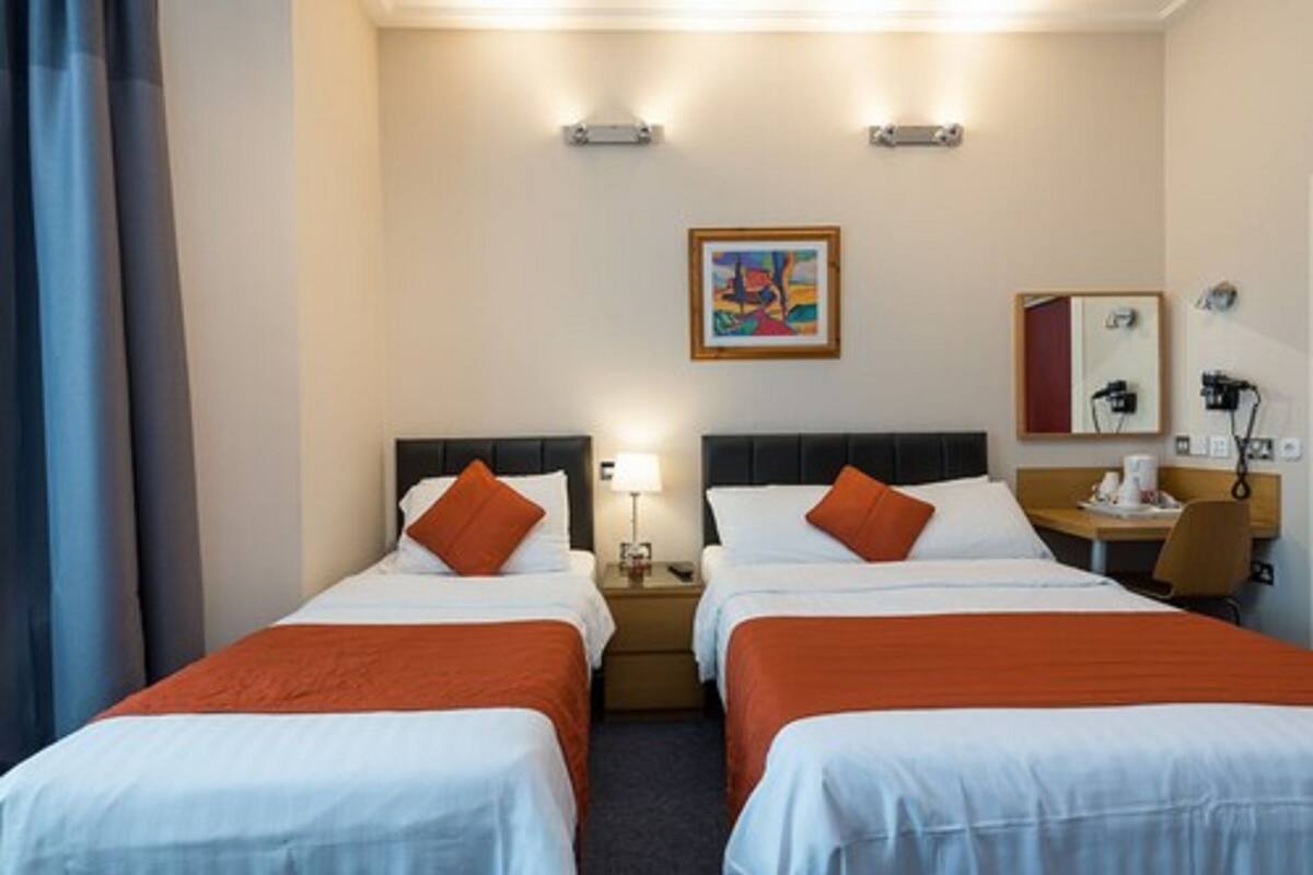 Una camera d'albergo con due letti, una scrivania, una sedia, una lampada, un quadro appeso al muro e un telefono.