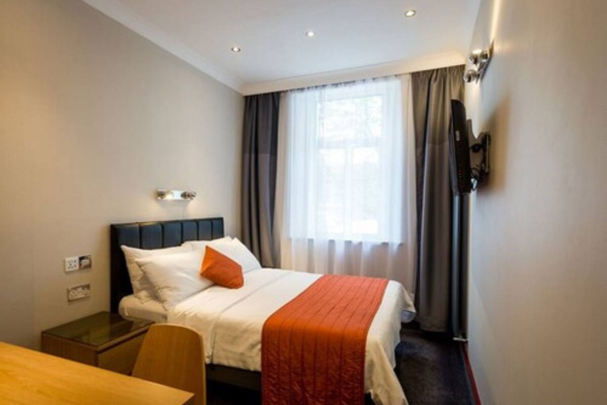 Una camera d'albergo con un letto, una scrivania, una sedia, una televisione e una finestra con tende.