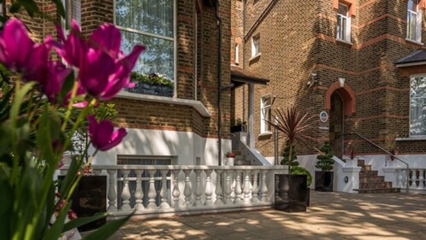 A courtyard with a brick building, a white balustrade, and a potted plant. - Adria Hotel (London)