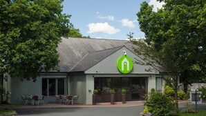 Un bâtiment avec un logo vert, des places assises à l’extérieur et un parking.