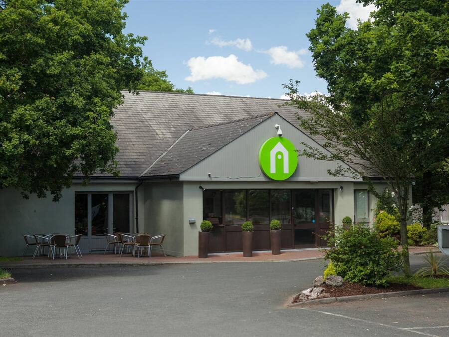 A building with a green logo, outdoor seating, and a parking lot.